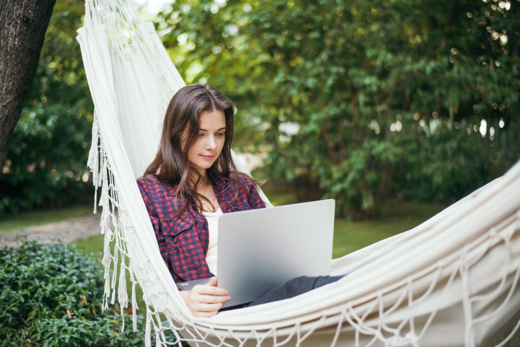 Young woman lying on hammock with a laptop